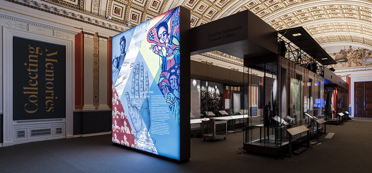 Image of a large exhibition featuring an electronic display and prized artificts within a large hall with decorated barrel vault ceiling.