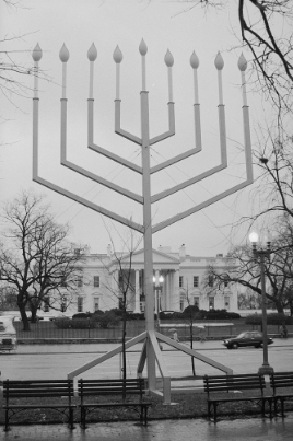 A large, 9-branch menorah is in the foreground with the White House in the background.